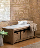 Wooden bench with storage baskets and folded blankets against a stone wall.