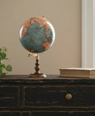 Vintage-style globe on a wooden dresser with a plant and book in the background.