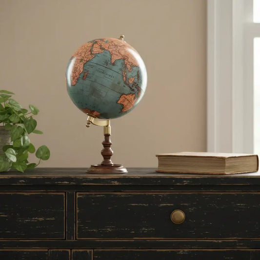Vintage-style globe on a wooden dresser with a plant and book in the background.