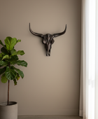 Bull skull wall decoration next to a potted plant on a neutral wall.