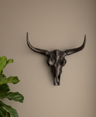 Decorative bull skull wall art on a beige wall with a plant to the left.