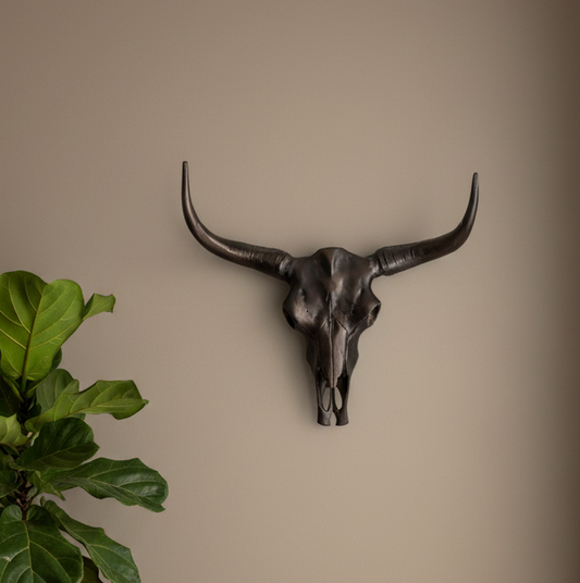 Decorative bull skull wall art on a beige wall with a plant to the left.