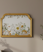 Decorative wall mirror with floral design and gold frame on a beige wall.