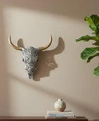 Decorative cow skull on a wall with a plant and small vase on a shelf below.