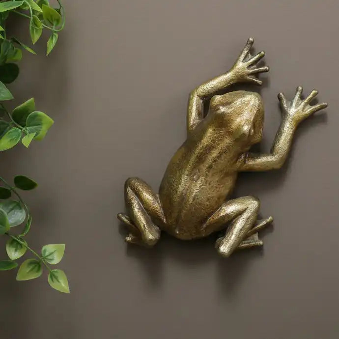 Bronze frog sculpture on a brown background with green leaves