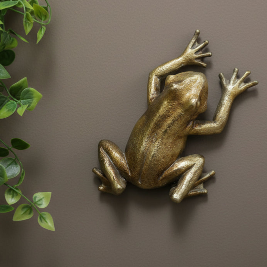 Bronze frog sculpture on a brown background with green leaves