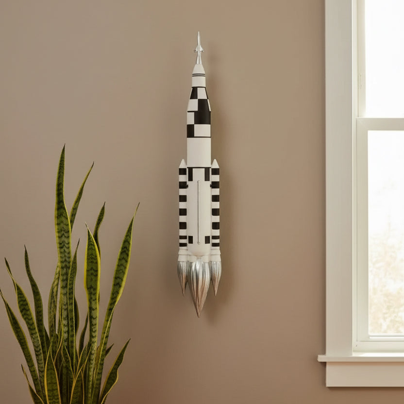 Decorative wall art resembling a rocket on a beige wall with a plant and window in the foreground.