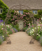 Wrought iron archway in a garden with colorful flowers and a house in the background