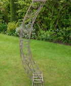 Decorative metal garden archway on a grassy lawn with greenery in the background