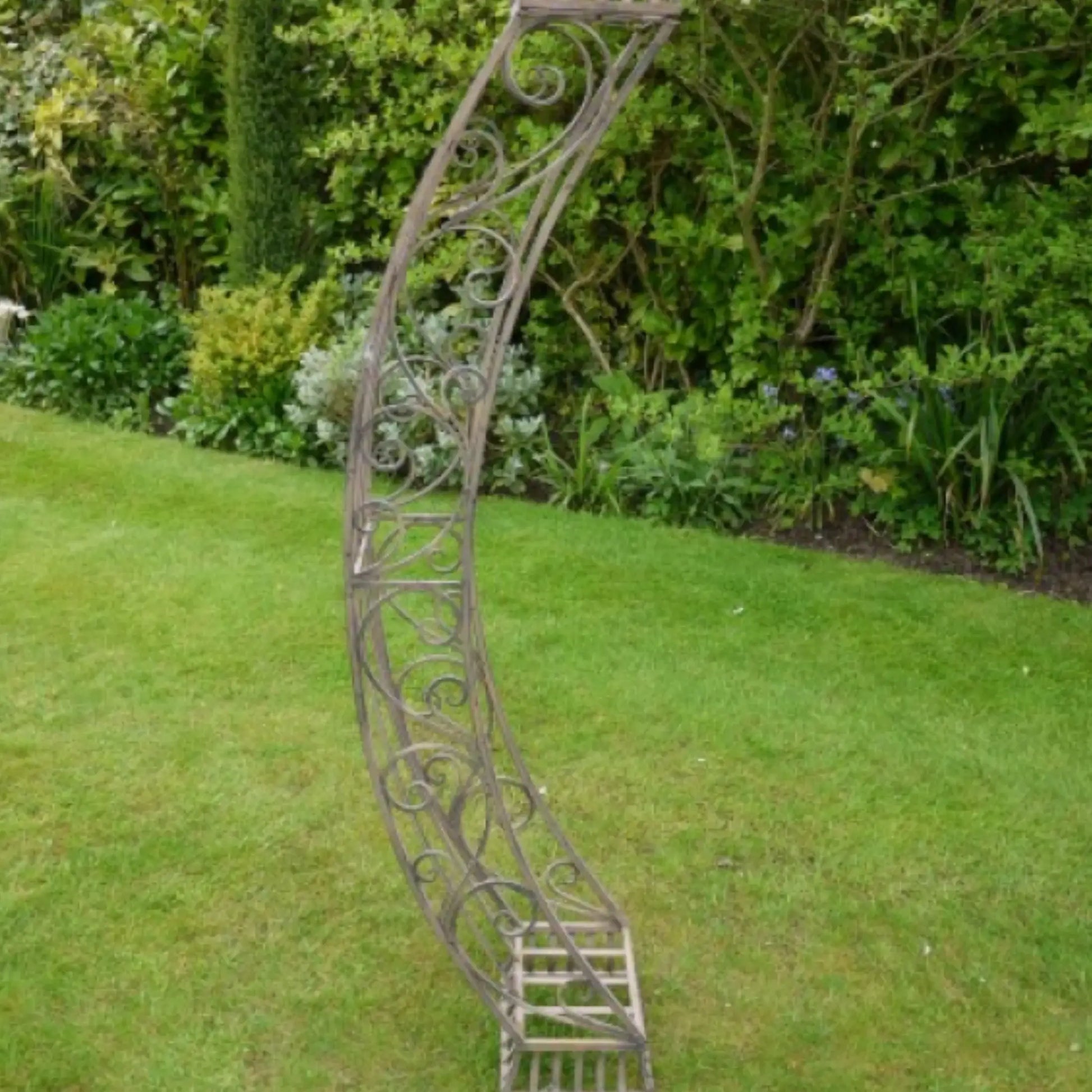 Decorative metal garden archway on a grassy lawn with greenery in the background