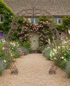 Decorative metal archway in a garden with flowers and a house in the background