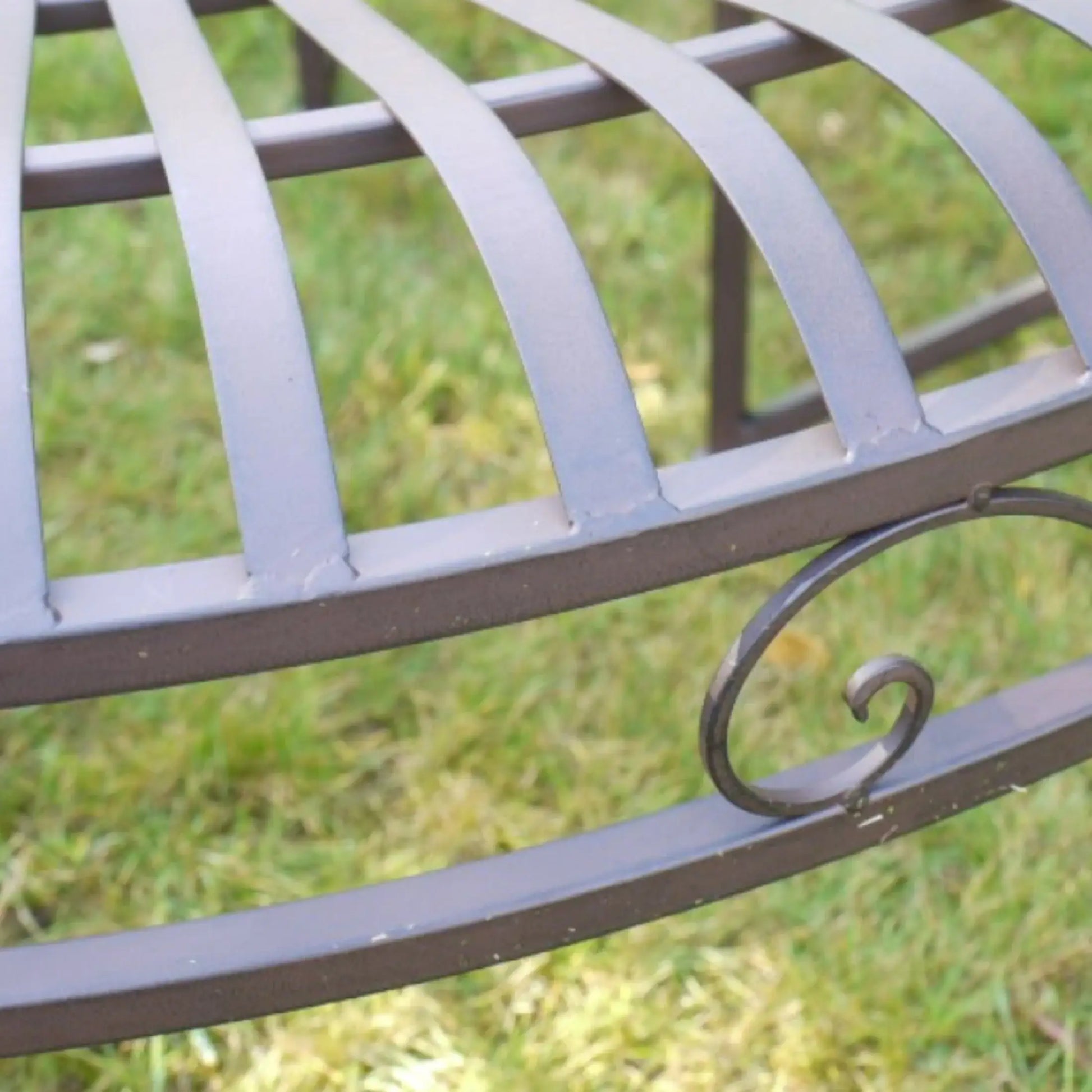 Metal garden bench with decorative armrest on a grassy background