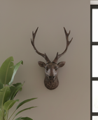 Decorative deer head mounted on a wall with a plant in the foreground.