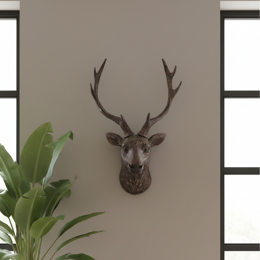 Decorative deer head mounted on a wall with a plant in the foreground.