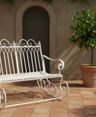 White metal bench on a patio with a potted tree and lavender plant.