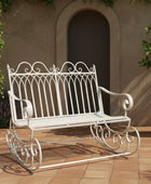 White metal garden bench on a patio with a building and plant in the background