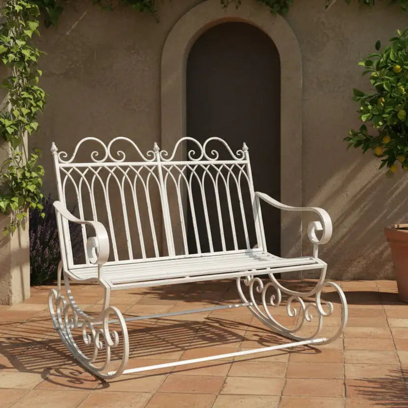 White metal garden bench on a patio with a building and plant in the background