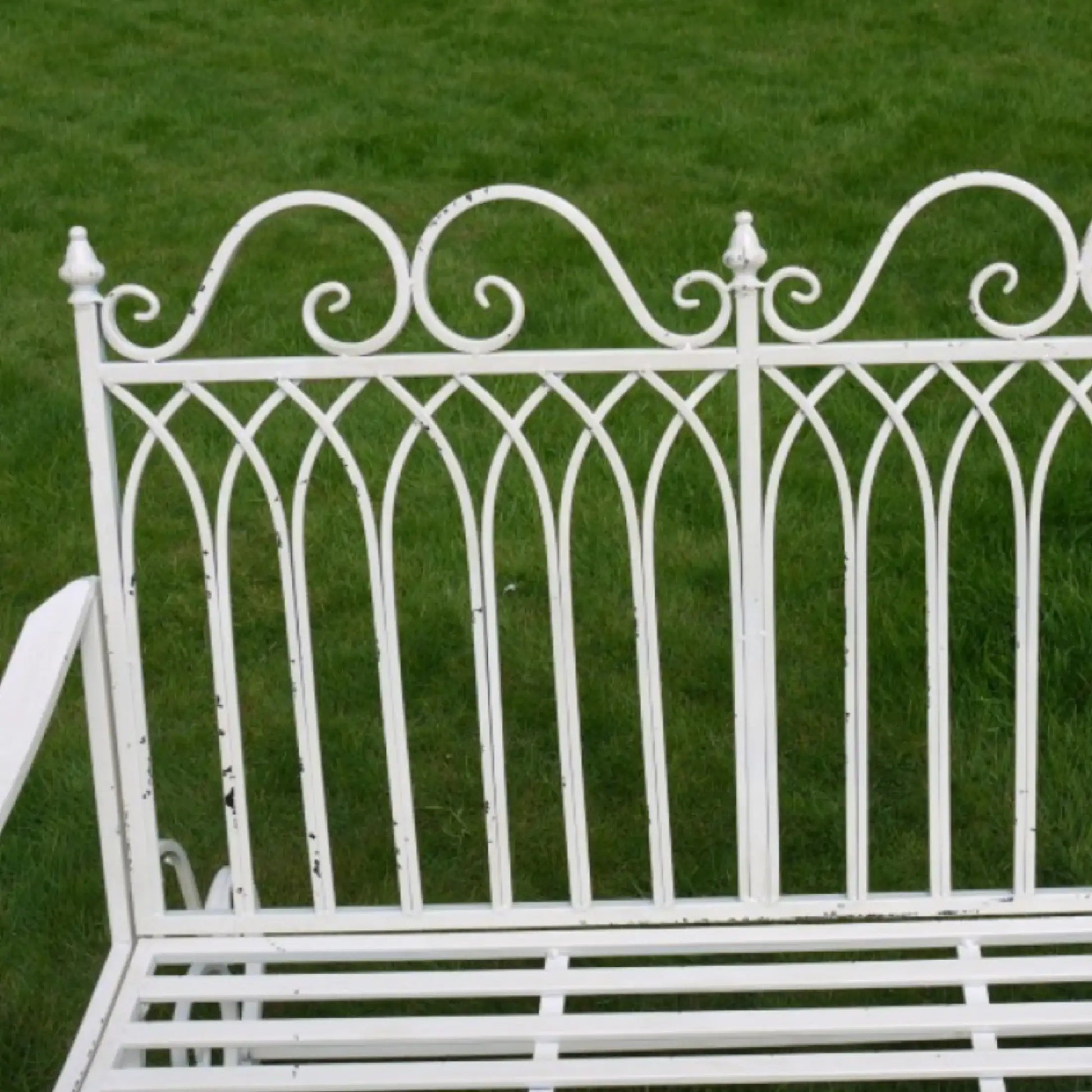 White metal bench with decorative backrest on a grassy background
