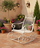 White ornate rocking chair on a patio with potted plants and flowers.