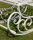 White metal garden bench with decorative scrollwork on a grassy background