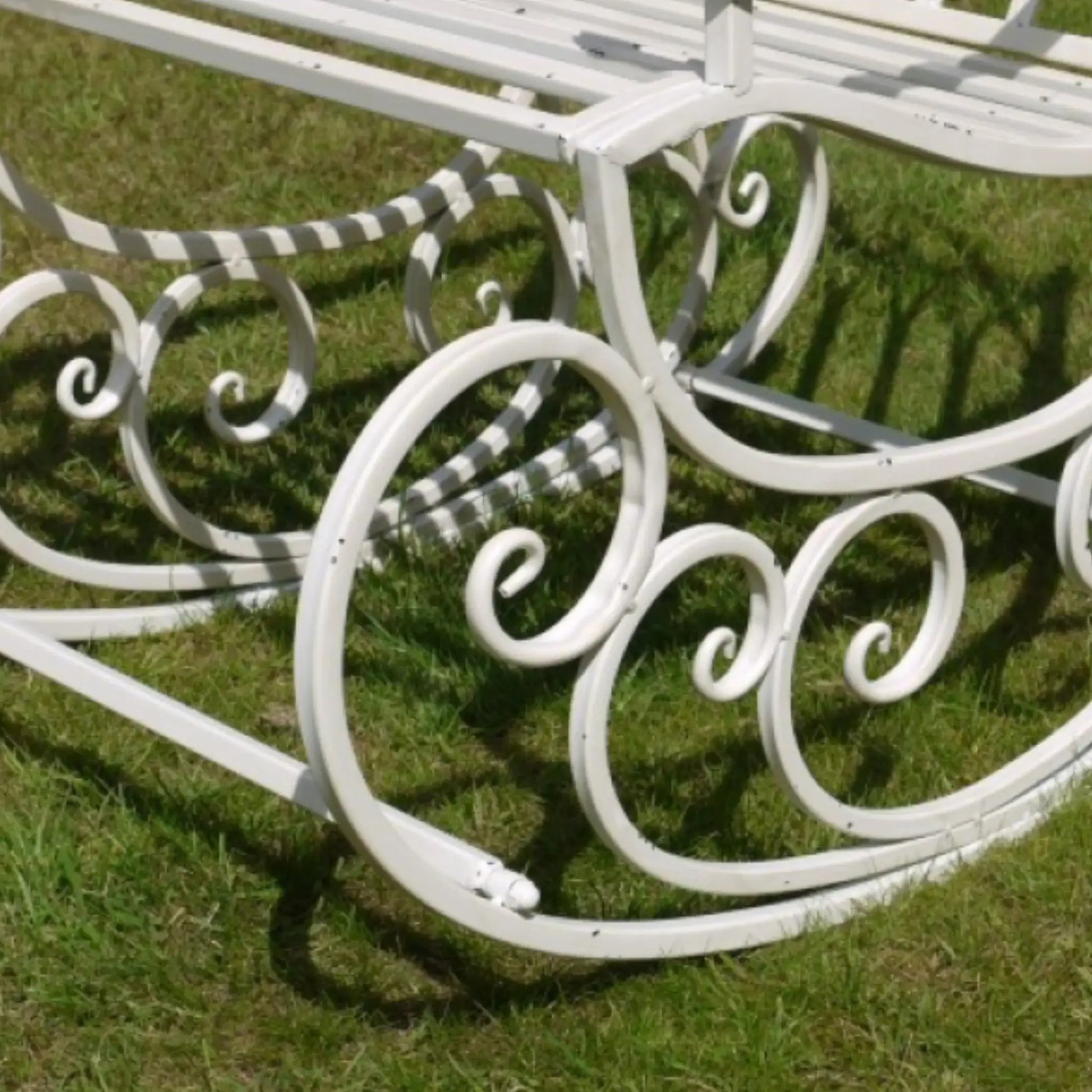 White metal garden bench with decorative scrollwork on a grassy background