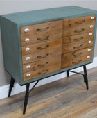 Wooden dresser with green top and black legs on a wooden floor.