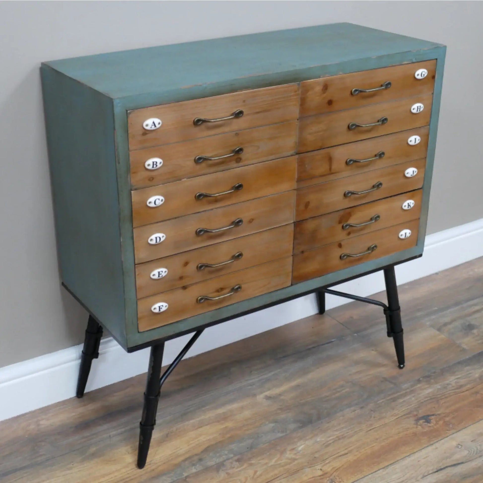 Wooden dresser with green top and black legs on a wooden floor.