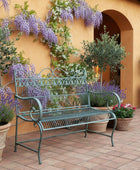 Decorative metal garden bench on a paved patio with greenery in the background