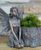 Bronze fairy statue with a planter shaped like a tree stump on a wooden surface.