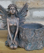 Bronze fairy statue with a tree stump planter against a stone wall background