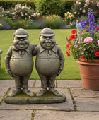 Two stone statues of men standing together in a garden with flowers and plants.