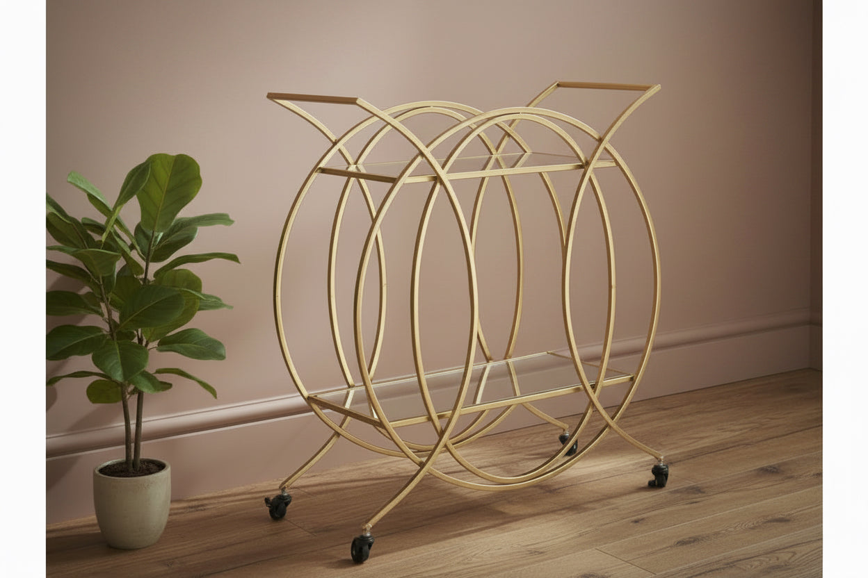 Gold circular magazine rack on wheels next to a plant against a beige wall.