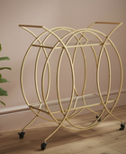 Gold circular bar cart on wheels against a beige wall with a plant to the left.