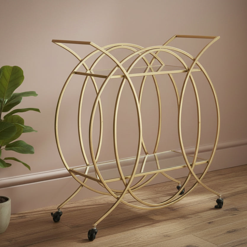 Gold circular bar cart on wheels against a beige wall with a plant to the left.