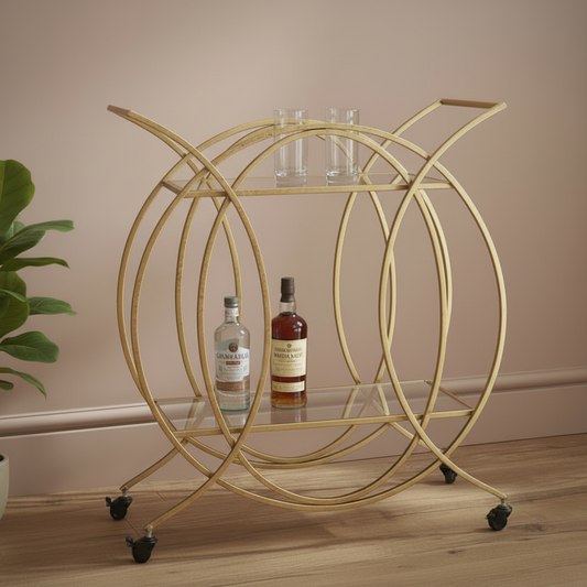 Gold circular bar cart with bottles and glasses on a wooden floor.