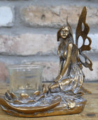 Bronze fairy figurine with a glass candle holder on a wooden surface.