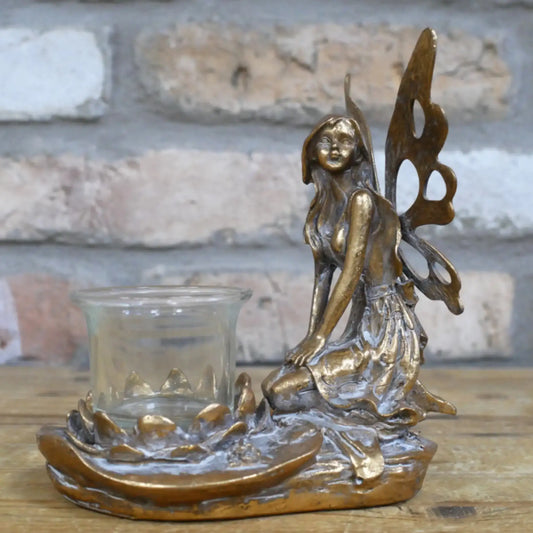 Bronze fairy figurine with a glass candle holder on a wooden surface.