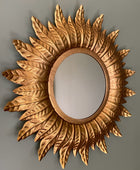 Decorative sunburst mirror with intricate details on a plain background
