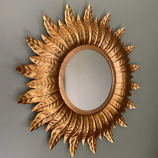 Decorative sunburst mirror with intricate details on a plain background