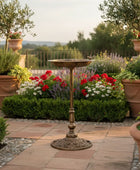Decorative bird bath in a garden setting with potted plants and flowers.