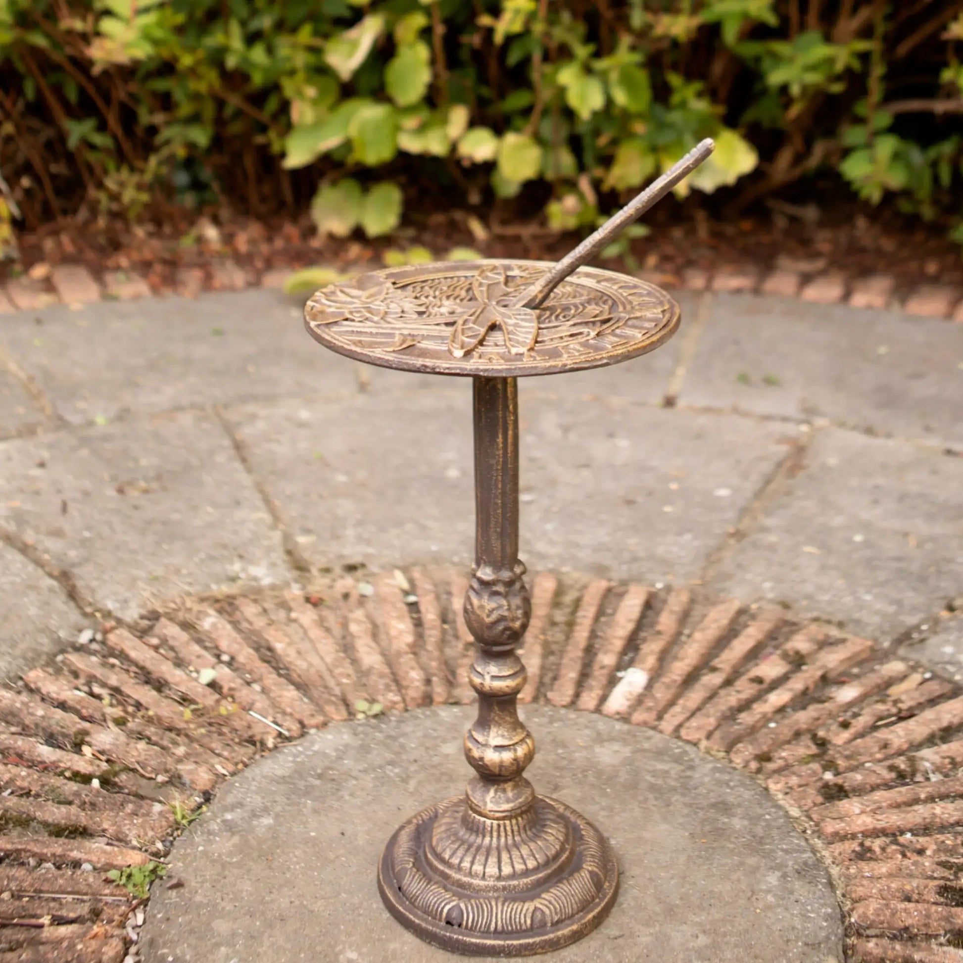 Decorative bronze sundial on a stone pedestal outdoors.