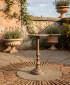 Decorative garden table with ornate design in a garden setting with stone walls and lavender plants.