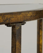 Close-up detail of a distressed gold and dark brown metal table frame, showing the corner joint and leg construction against a light gray background.