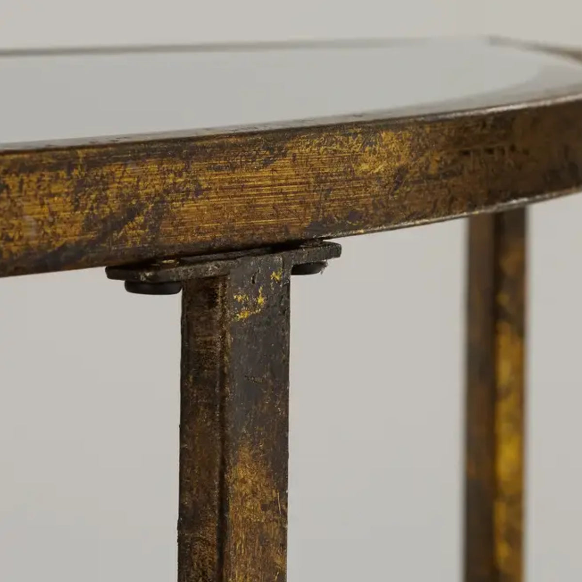 Close-up detail of a distressed gold and dark brown metal table frame, showing the corner joint and leg construction against a light gray background.