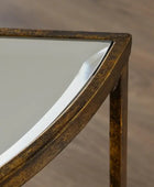 Close-up of a corner of a mirrored table with a distressed gold and bronze metal frame, set against a blurred wood floor background.
