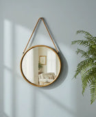 Round wall mirror with a rope hanging on a light blue wall next to a potted plant.
