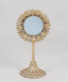 A decorative sunburst-style vanity mirror with a gold-toned frame and stand, photographed against a plain light gray studio background.