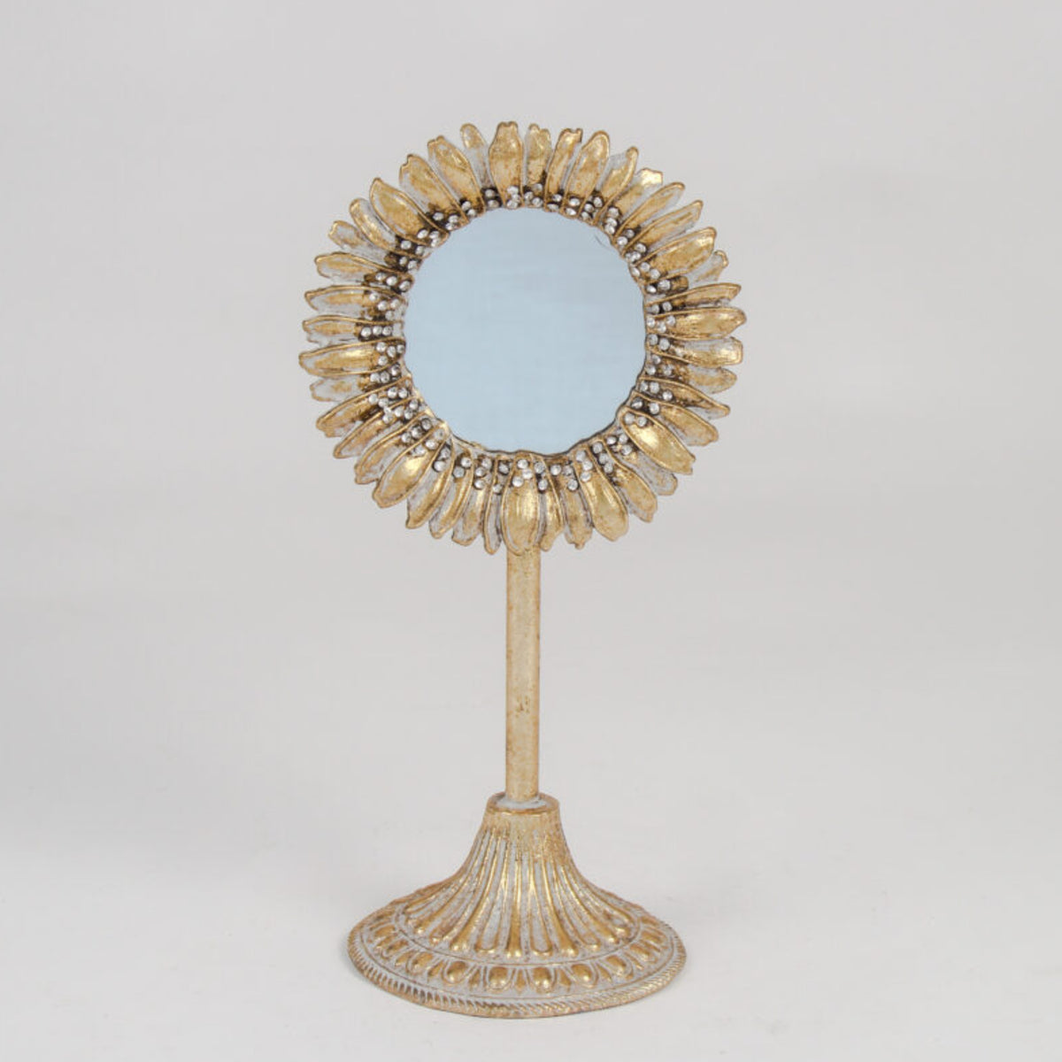 A decorative sunburst-style vanity mirror with a gold-toned frame and stand, photographed against a plain light gray studio background.