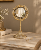 A decorative tabletop mirror with a sunburst frame and fluted pedestal base, styled on a distressed cream dresser against a warm taupe wall.
