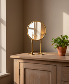 Gold vanity mirror on a wooden dresser with a plant in the background